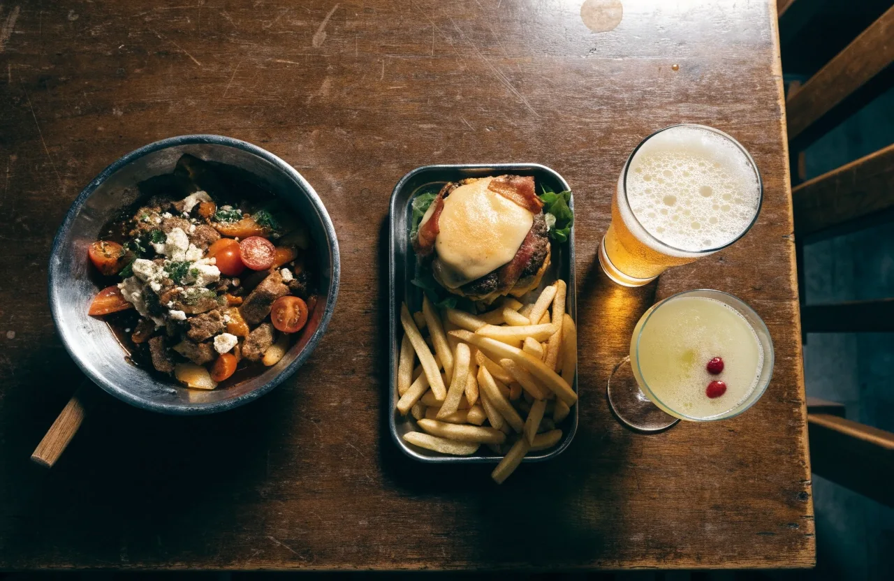 An overhead table of shared appetizers, a burger and fries, a pint and a mocktail at a sports bar