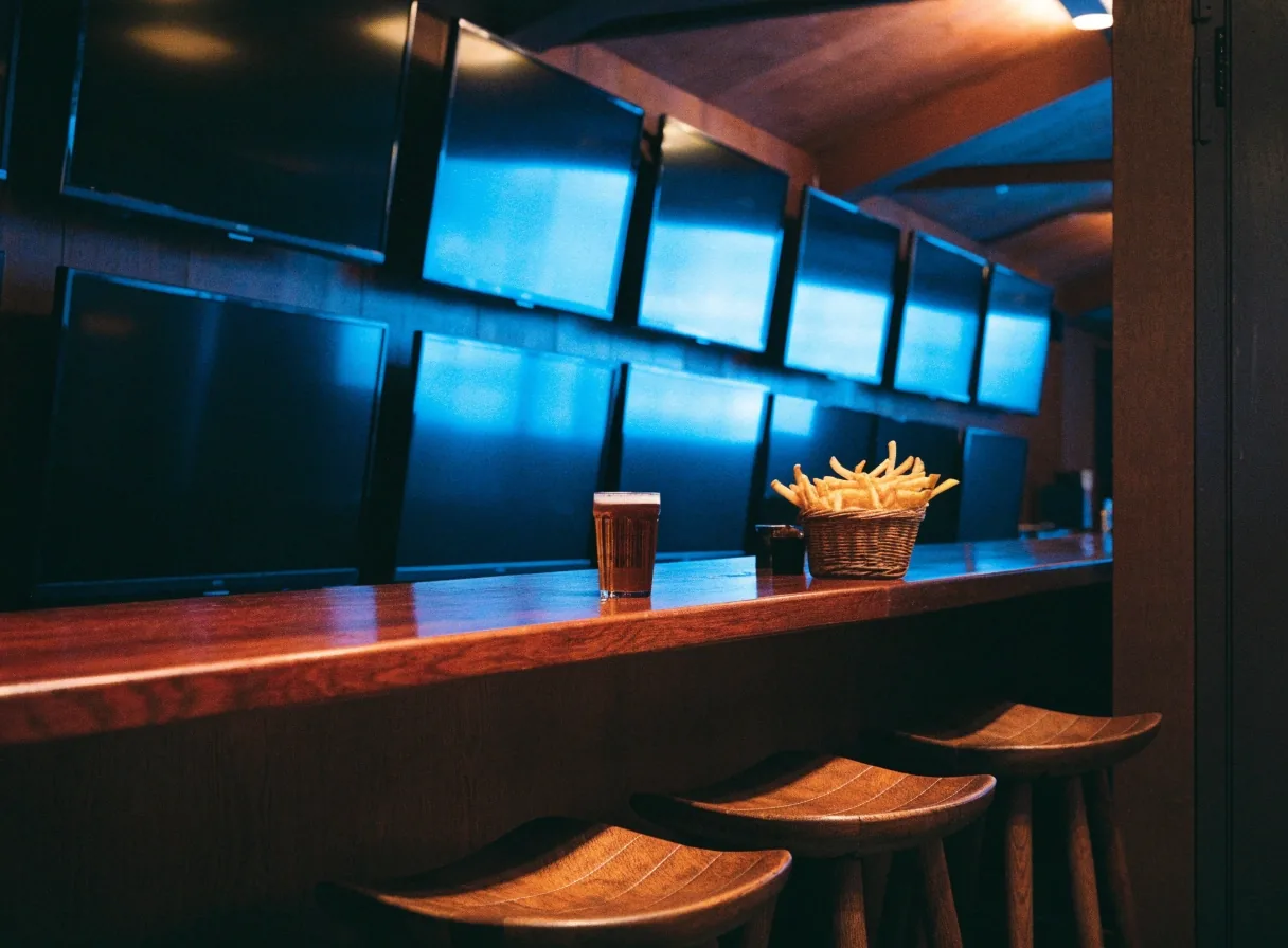 A television-lit corner of the bar with stools and an untouched order